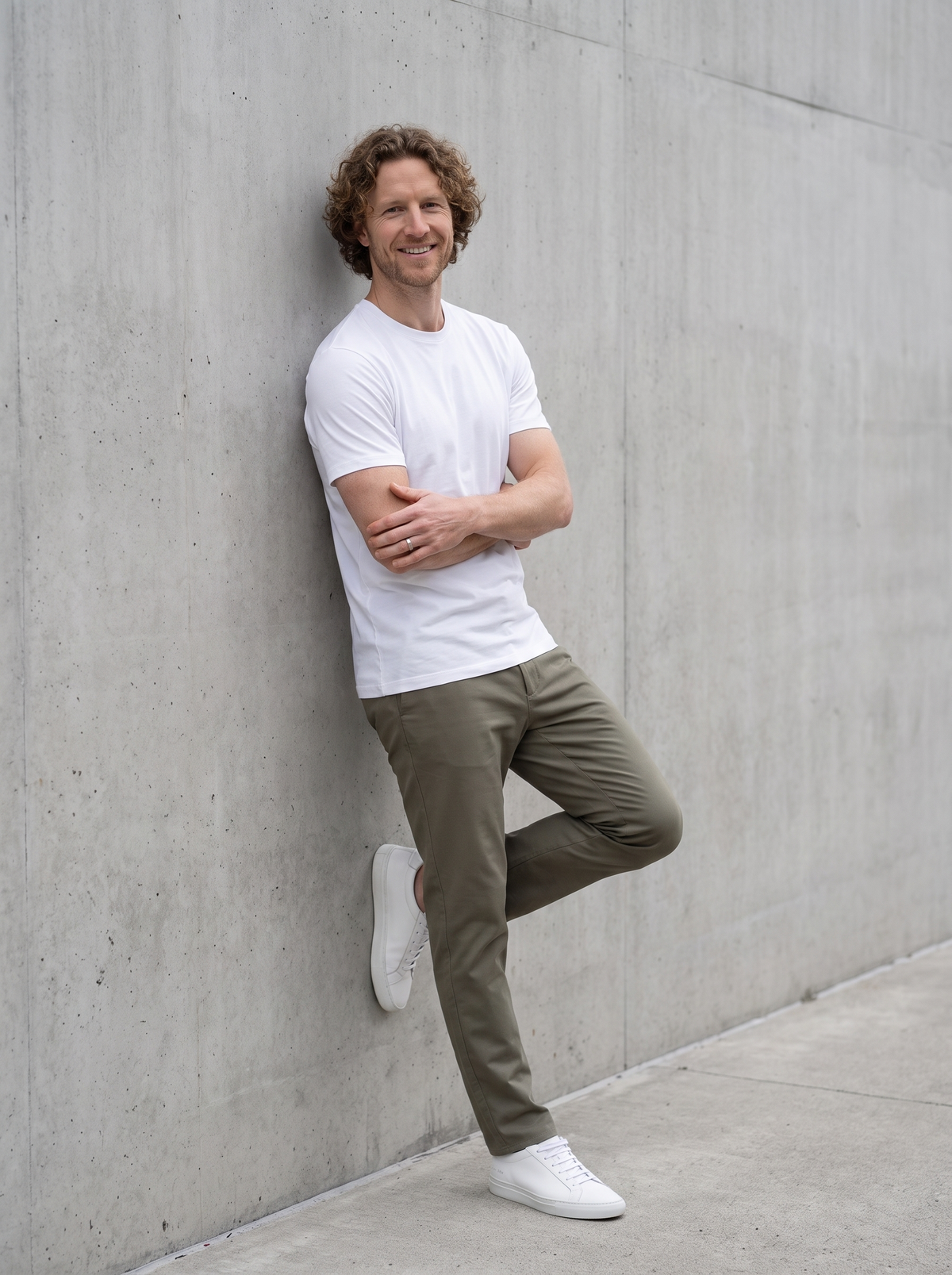 Man wearing a white SOLOS crewneck T-shirt leaning against a concrete wall in natural daylight