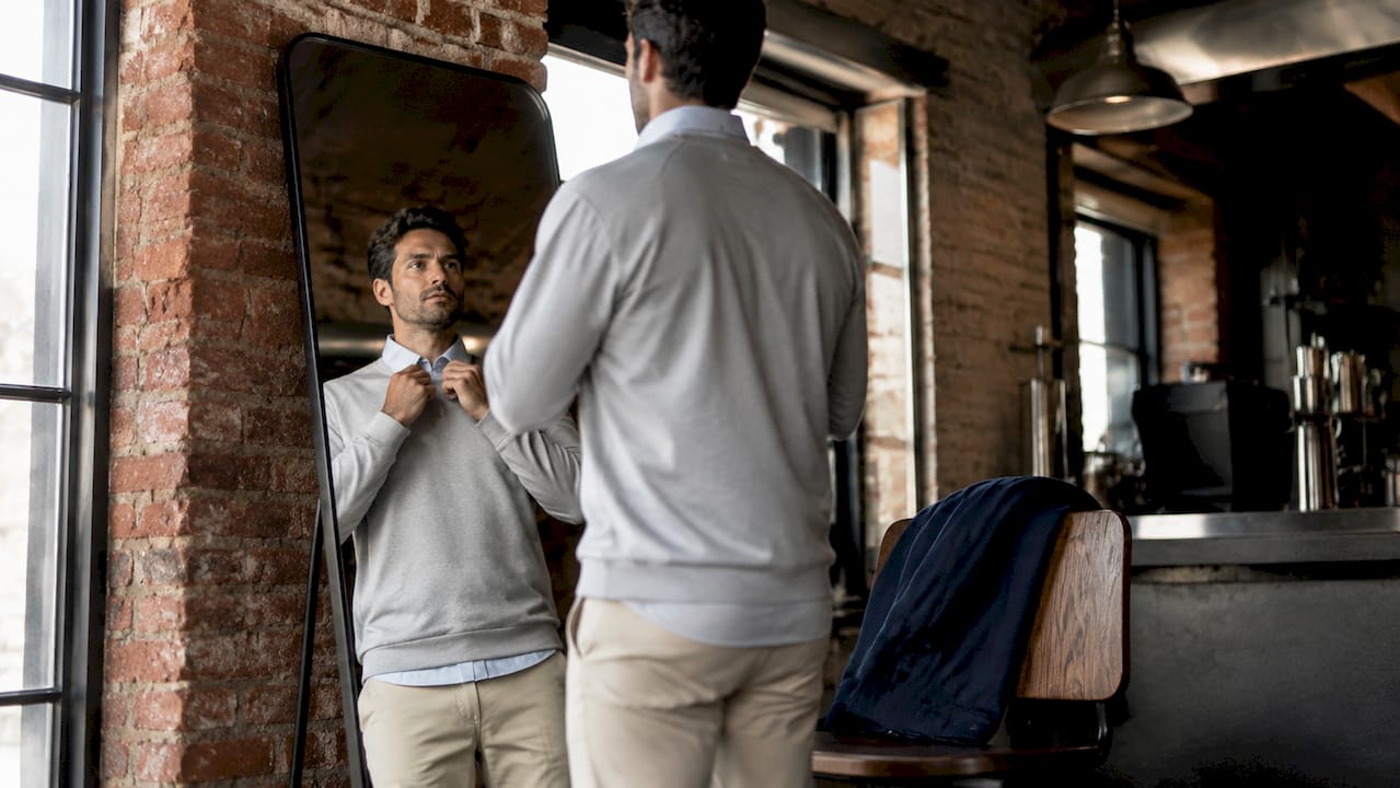 Man layering cotton shirt and pullover indoors