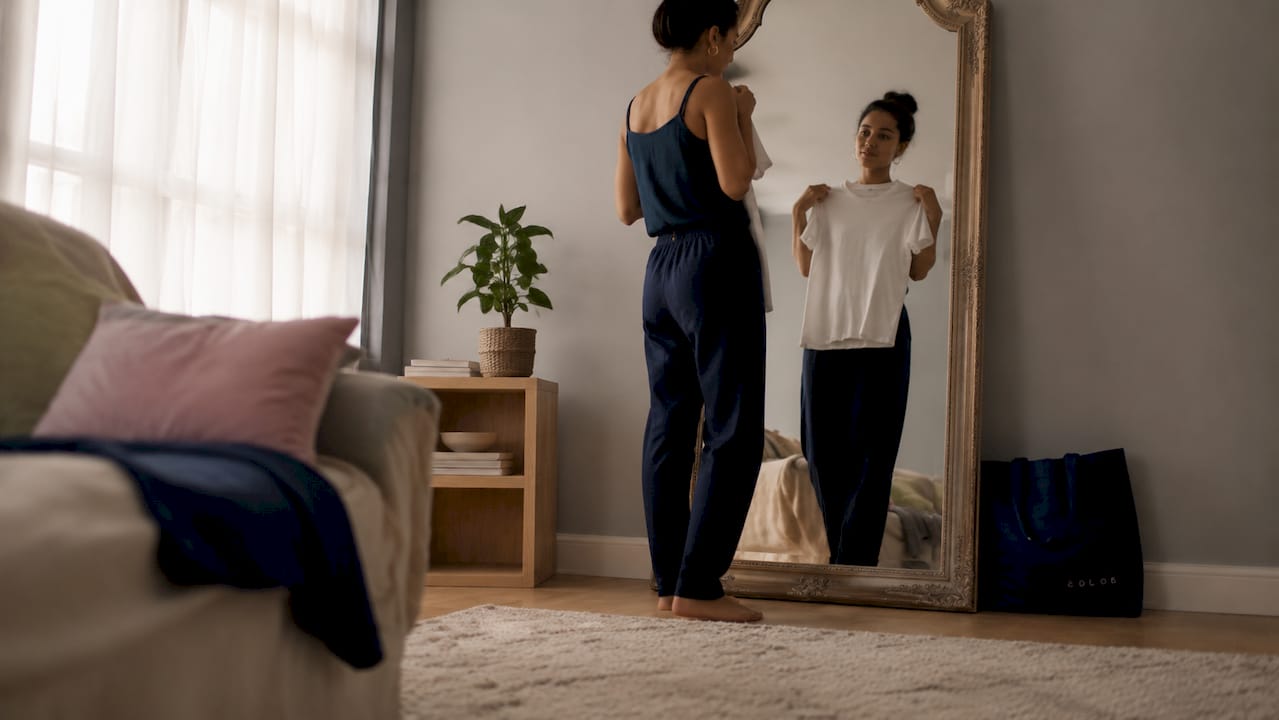 Woman holding white cotton t-shirt in bedroom mirror
